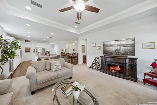 carpeted living room featuring a raised ceiling, ceiling fan, and crown molding