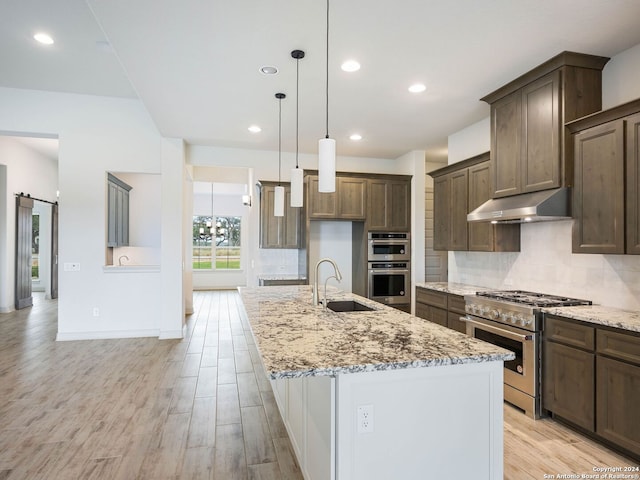 kitchen featuring appliances with stainless steel finishes, light wood-type flooring, light stone counters, sink, and an island with sink