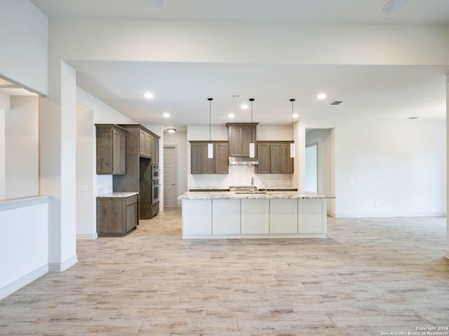 kitchen featuring stainless steel oven, a center island with sink, decorative backsplash, decorative light fixtures, and light stone counters