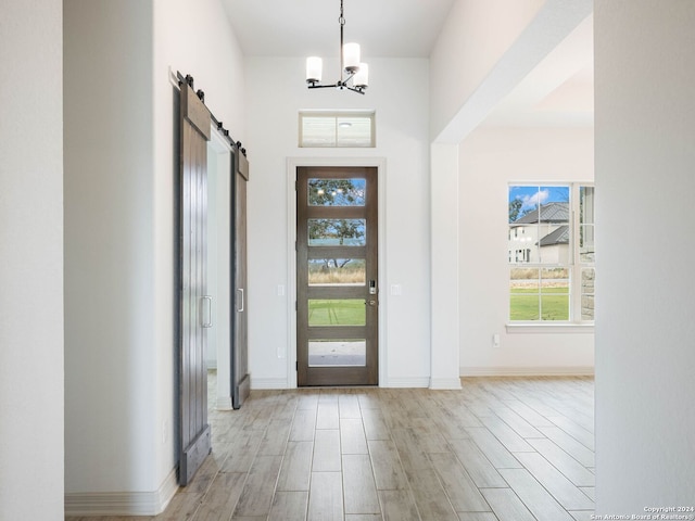 entryway with a barn door, light hardwood / wood-style floors, and a notable chandelier