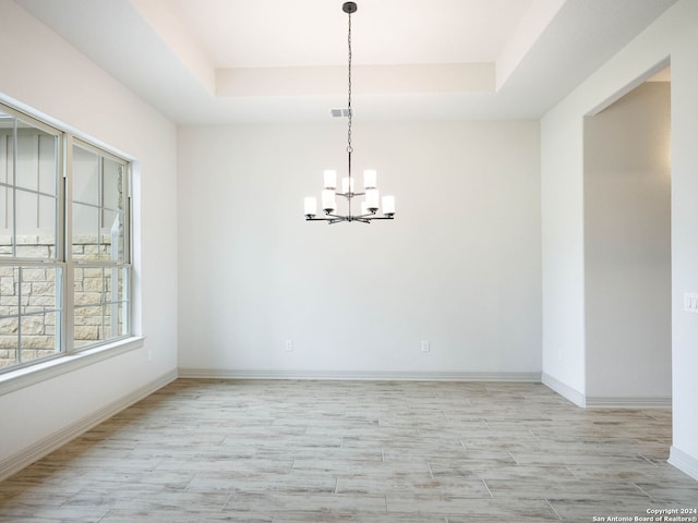 empty room featuring a raised ceiling, light hardwood / wood-style floors, and a notable chandelier