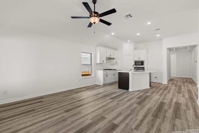 kitchen with a kitchen island with sink, visible vents, white cabinetry, light countertops, and stainless steel microwave