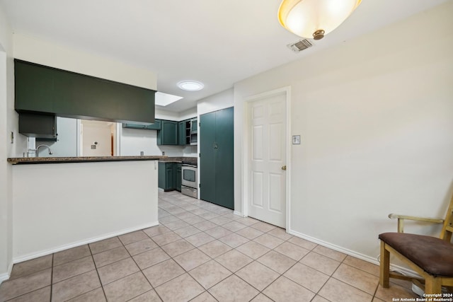 kitchen with dark stone counters, sink, light tile patterned floors, stainless steel range oven, and kitchen peninsula