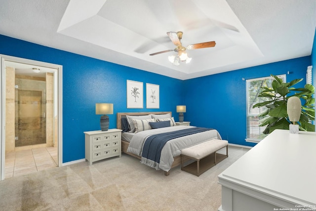 carpeted bedroom featuring a textured ceiling, ensuite bathroom, ceiling fan, and a tray ceiling