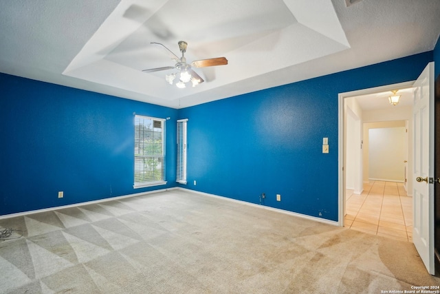 carpeted empty room featuring a raised ceiling, ceiling fan, and a textured ceiling