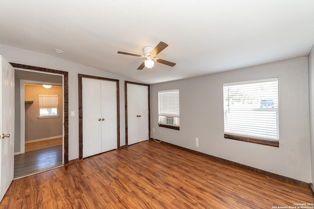 unfurnished bedroom featuring dark hardwood / wood-style floors, multiple windows, multiple closets, and ceiling fan