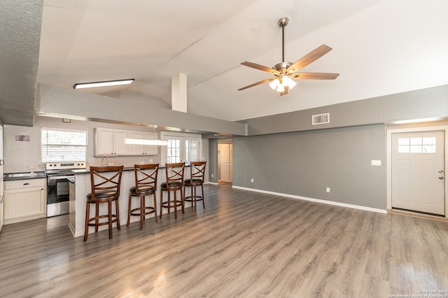 kitchen featuring ceiling fan, white cabinetry, a kitchen breakfast bar, stainless steel range with electric cooktop, and hardwood / wood-style flooring