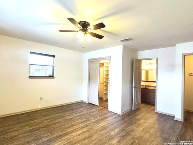 unfurnished bedroom with ensuite bathroom, a walk in closet, ceiling fan, dark hardwood / wood-style flooring, and a closet