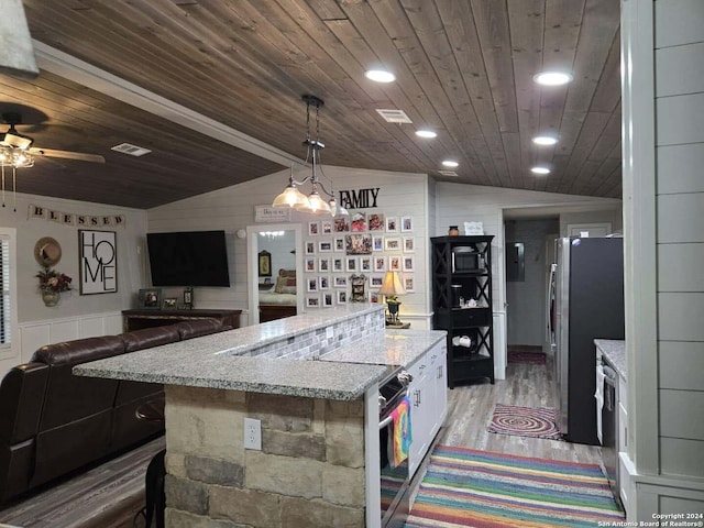 kitchen featuring hardwood / wood-style floors, a center island, vaulted ceiling, white cabinetry, and stainless steel refrigerator