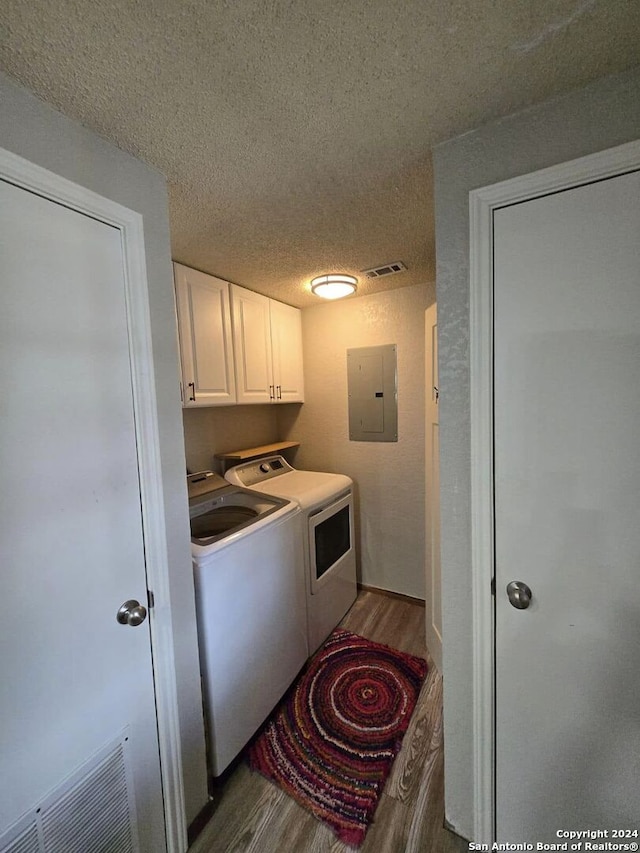 clothes washing area featuring wood-type flooring, a textured ceiling, electric panel, and washer and clothes dryer