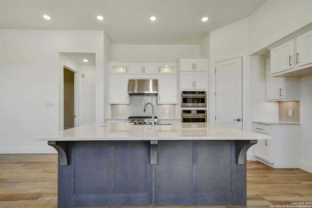 kitchen with stainless steel double oven, ventilation hood, light hardwood / wood-style flooring, and a spacious island