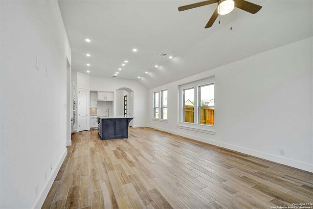 unfurnished living room featuring ceiling fan, sink, vaulted ceiling, and light wood-type flooring