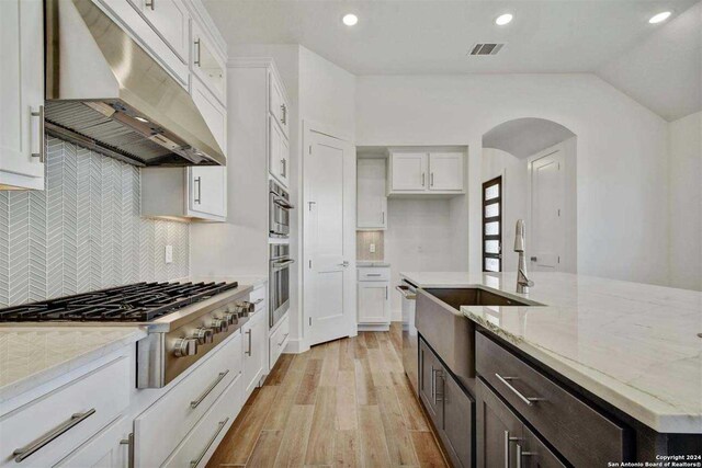 kitchen featuring appliances with stainless steel finishes, light wood-type flooring, tasteful backsplash, light stone counters, and white cabinetry