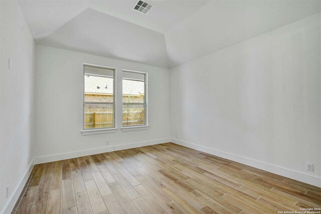 empty room featuring light wood-type flooring, vaulted ceiling, and a tray ceiling