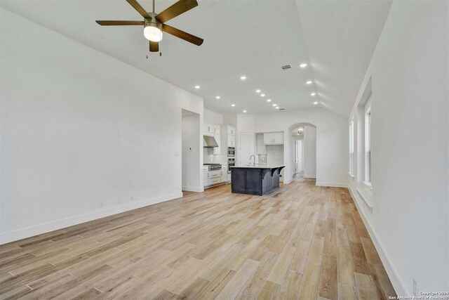 unfurnished living room with ceiling fan, vaulted ceiling, sink, and light hardwood / wood-style flooring