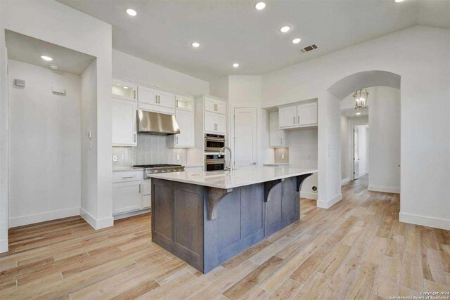 kitchen with white cabinets, a kitchen bar, stainless steel appliances, a kitchen island with sink, and light hardwood / wood-style flooring