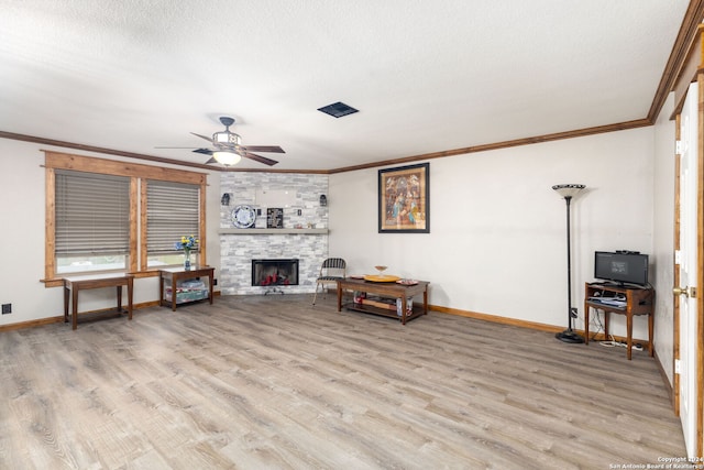 living area featuring ceiling fan, a stone fireplace, light wood-type flooring, and a textured ceiling