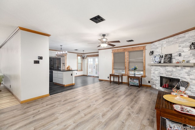 living room featuring a stone fireplace, crown molding, light hardwood / wood-style flooring, and ceiling fan with notable chandelier