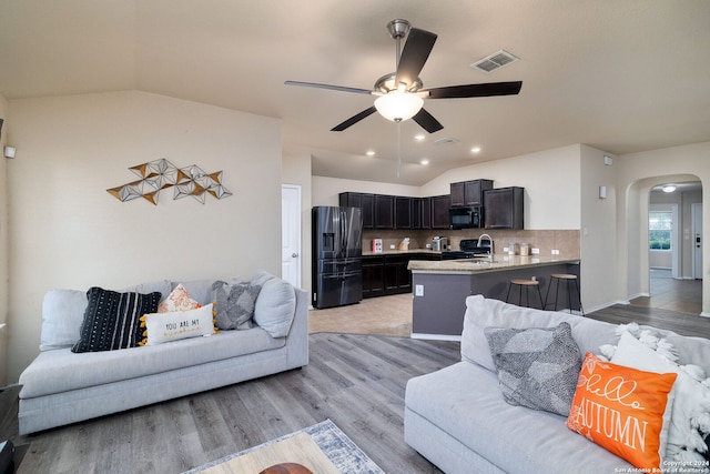 living room featuring ceiling fan, sink, light hardwood / wood-style floors, and vaulted ceiling