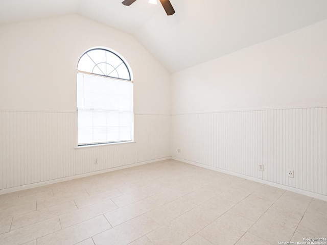 unfurnished room with light tile patterned floors, vaulted ceiling, ceiling fan, and wood walls