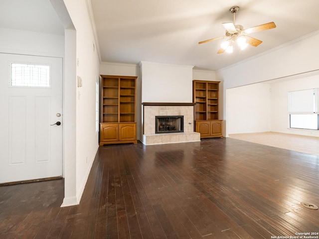 unfurnished living room with a tile fireplace, ceiling fan, dark hardwood / wood-style flooring, and crown molding