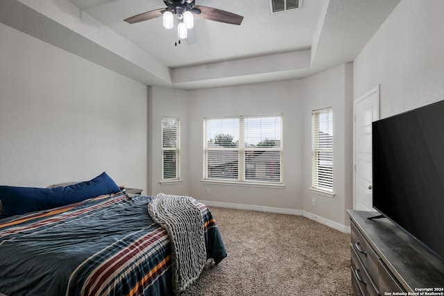 carpeted bedroom featuring a tray ceiling and ceiling fan