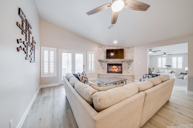 living room with ceiling fan, a stone fireplace, light wood-type flooring, and vaulted ceiling