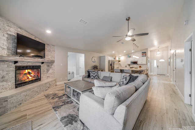 living room featuring a fireplace, light hardwood / wood-style flooring, vaulted ceiling, and ceiling fan