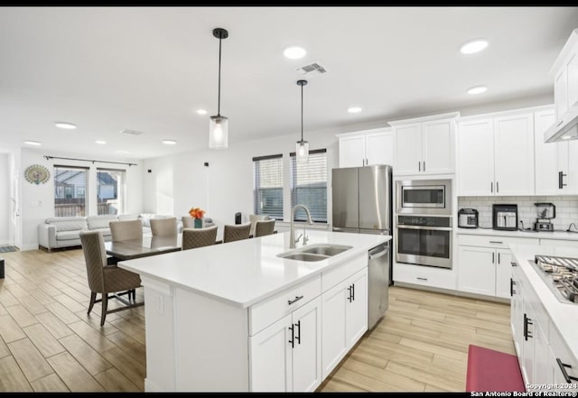 kitchen featuring sink, light hardwood / wood-style floors, pendant lighting, a kitchen island with sink, and appliances with stainless steel finishes