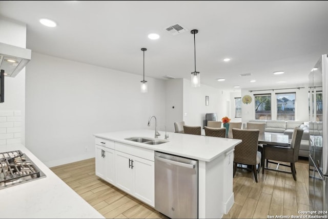 kitchen with appliances with stainless steel finishes, light wood-type flooring, sink, white cabinets, and hanging light fixtures