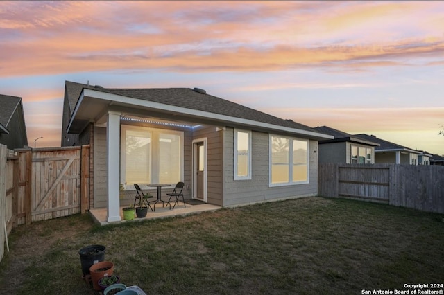 back house at dusk featuring a lawn and a patio