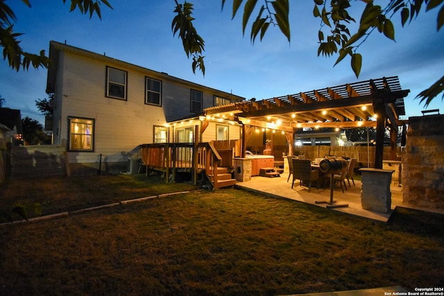 back house at dusk featuring a pergola, a wooden deck, a patio area, and a lawn