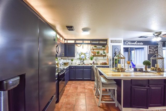 kitchen with ceiling fan, stainless steel appliances, a textured ceiling, a kitchen bar, and light tile patterned floors