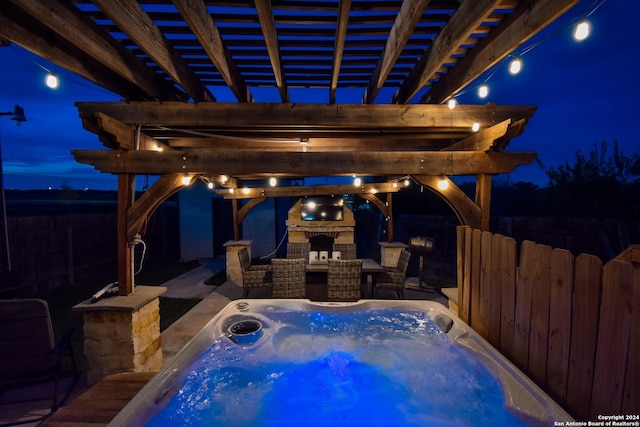 patio at night with a pergola, a hot tub, and an outdoor fireplace