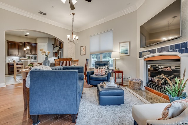 living room featuring ornamental molding, ceiling fan with notable chandelier, and light wood-type flooring