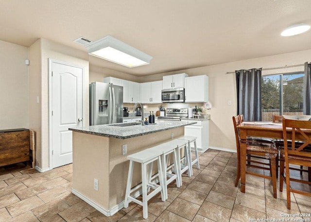 kitchen with a center island with sink, sink, light stone countertops, appliances with stainless steel finishes, and white cabinetry