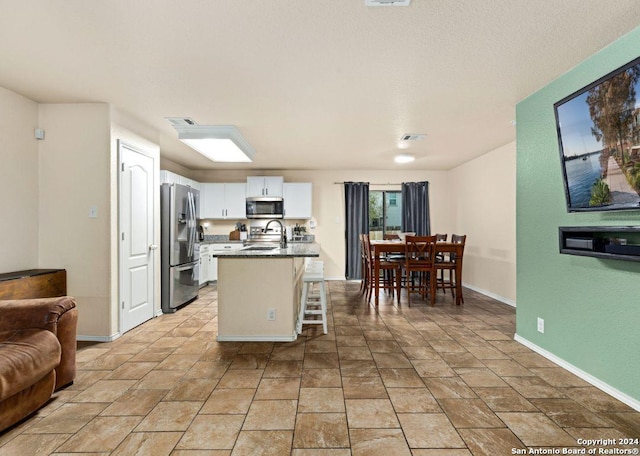 kitchen with a kitchen breakfast bar, white cabinets, an island with sink, and appliances with stainless steel finishes