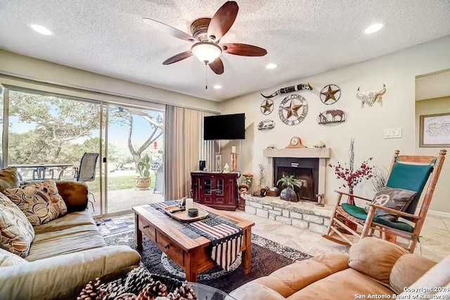 living room with a stone fireplace, ceiling fan, tile patterned flooring, and a textured ceiling