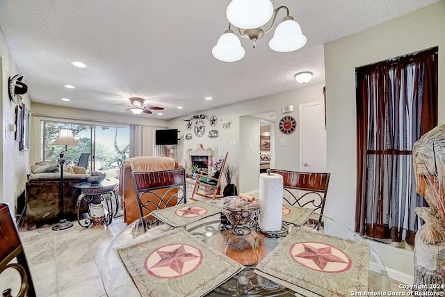 tiled dining area featuring a textured ceiling, a fireplace, and ceiling fan with notable chandelier