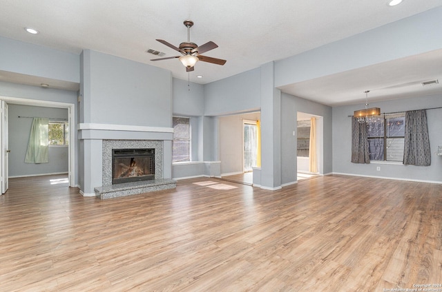 unfurnished living room with ceiling fan with notable chandelier, light wood-type flooring, and a high end fireplace