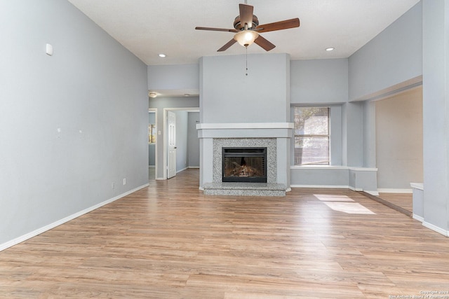 unfurnished living room with ceiling fan, light wood-type flooring, and a high ceiling