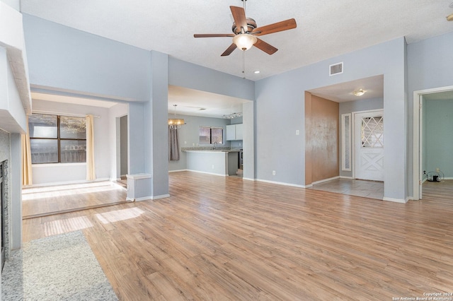 unfurnished living room with ceiling fan with notable chandelier, a textured ceiling, and light hardwood / wood-style flooring