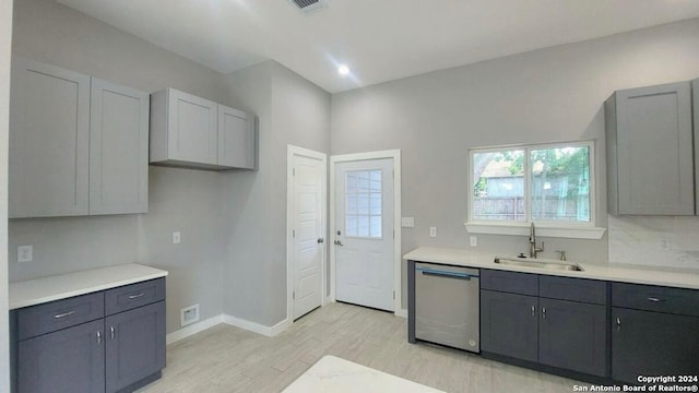 kitchen featuring stainless steel dishwasher, gray cabinets, light hardwood / wood-style floors, and sink