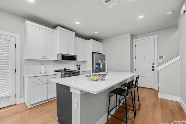 kitchen featuring a center island with sink, a kitchen breakfast bar, light hardwood / wood-style flooring, appliances with stainless steel finishes, and white cabinetry