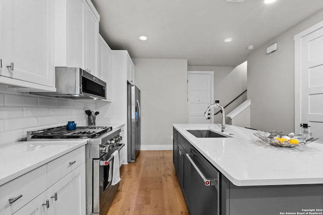 kitchen with stainless steel appliances, sink, light hardwood / wood-style flooring, white cabinetry, and an island with sink