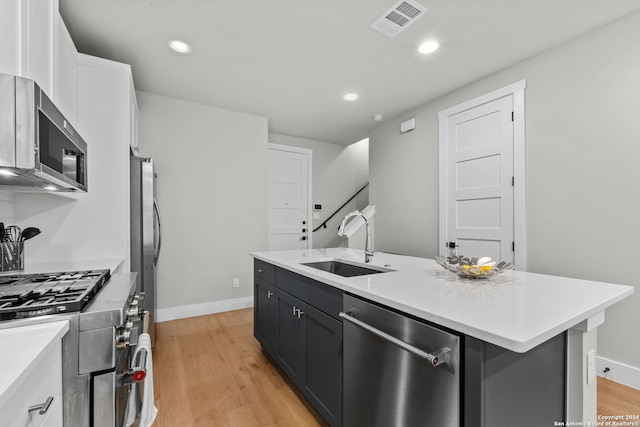 kitchen with stainless steel appliances, a kitchen island with sink, sink, light hardwood / wood-style floors, and white cabinetry