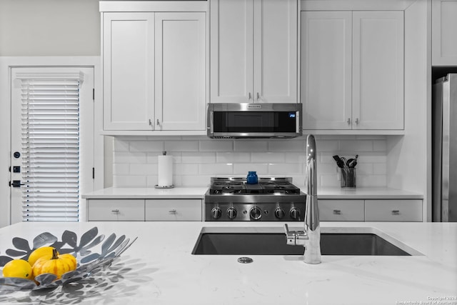 kitchen with tasteful backsplash, white cabinetry, light stone countertops, and appliances with stainless steel finishes