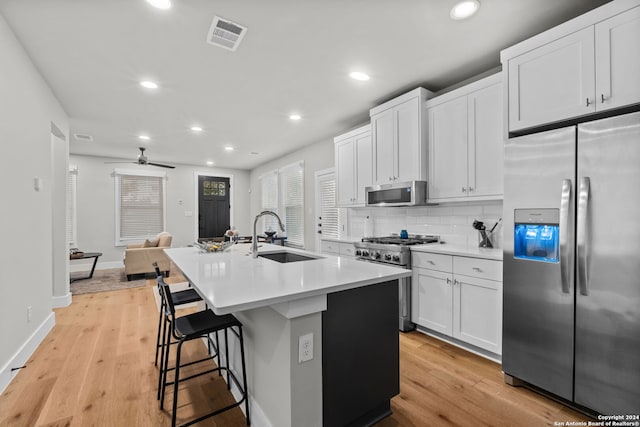 kitchen with stainless steel appliances, a kitchen island with sink, sink, white cabinets, and light hardwood / wood-style floors