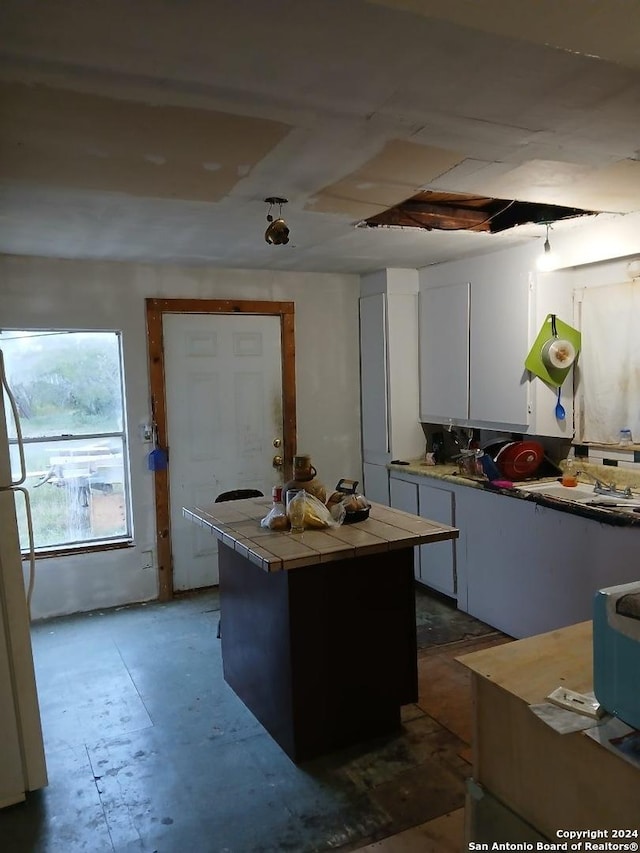 kitchen with tile countertops, white cabinetry, fridge, and a kitchen island