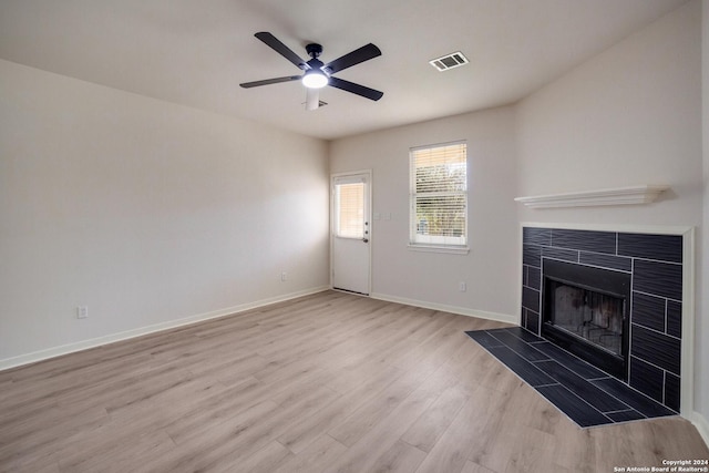 unfurnished living room with a tiled fireplace, ceiling fan, and light wood-type flooring